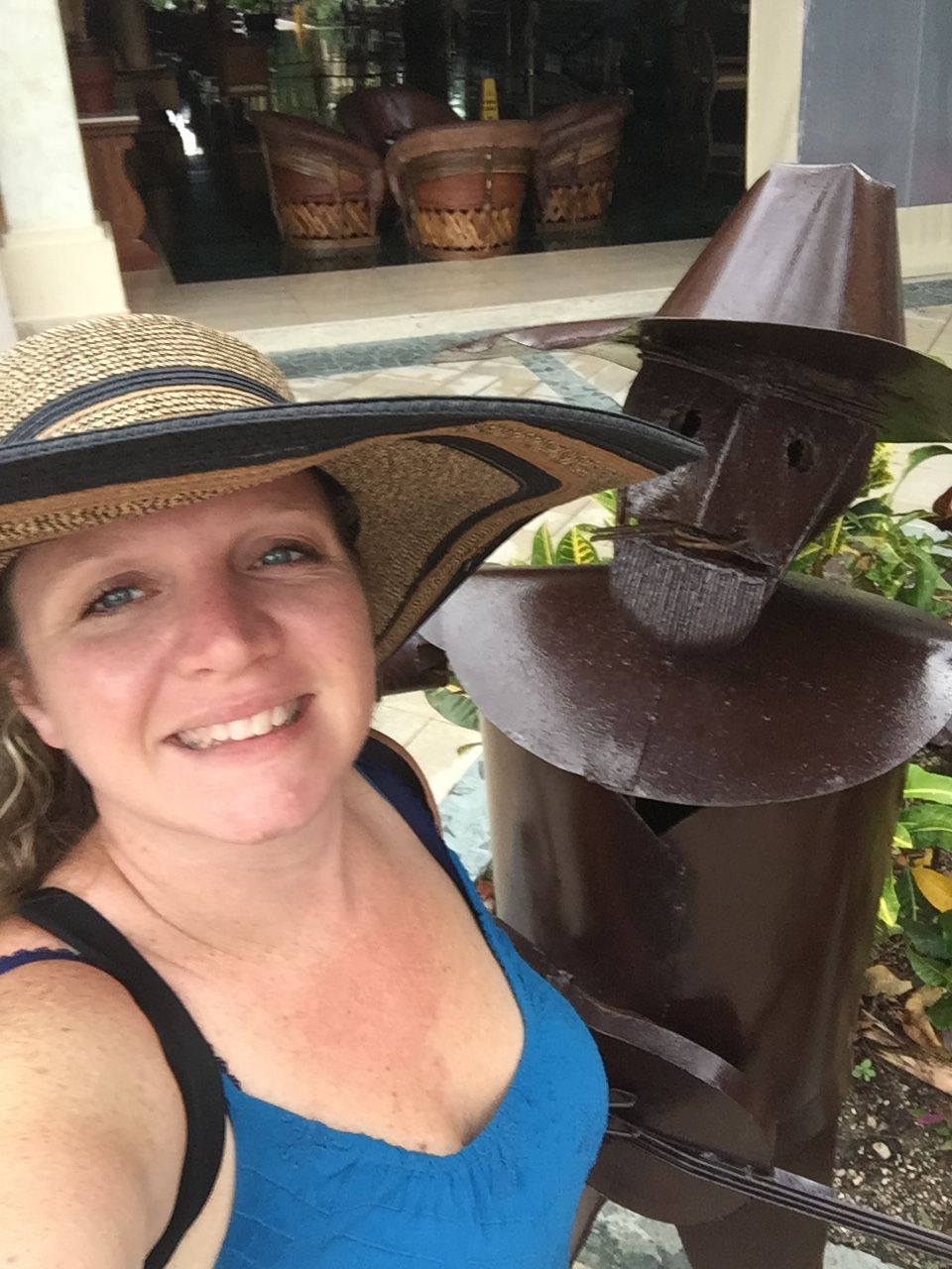 a woman in a wide-brimmed hat smiles for a selfie with a brown metal statue