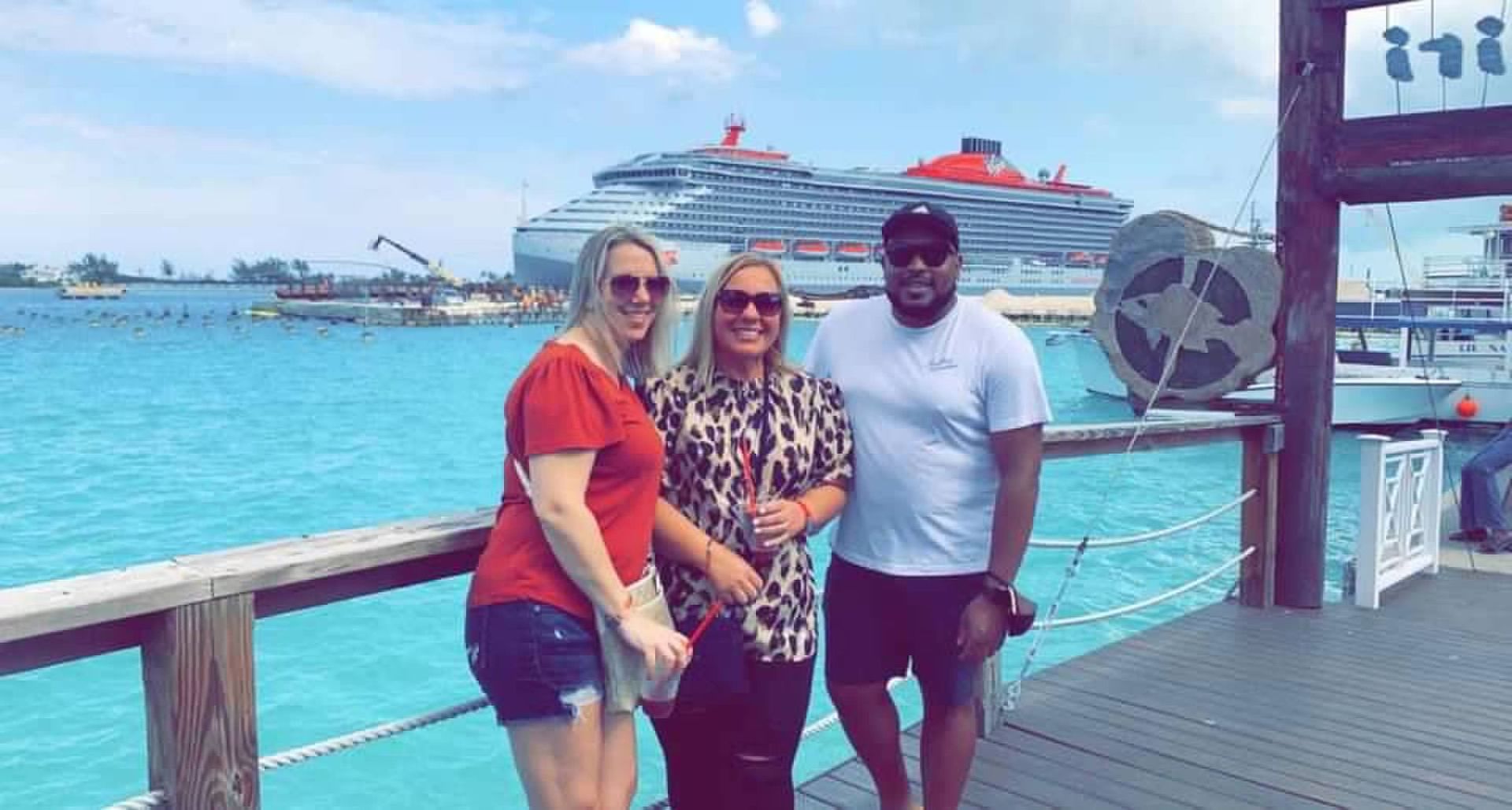 Three people are standing on a pier in front of a cruise ship