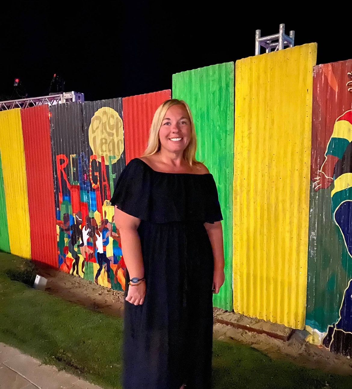 A woman in a black dress is standing in front of a colorful fence