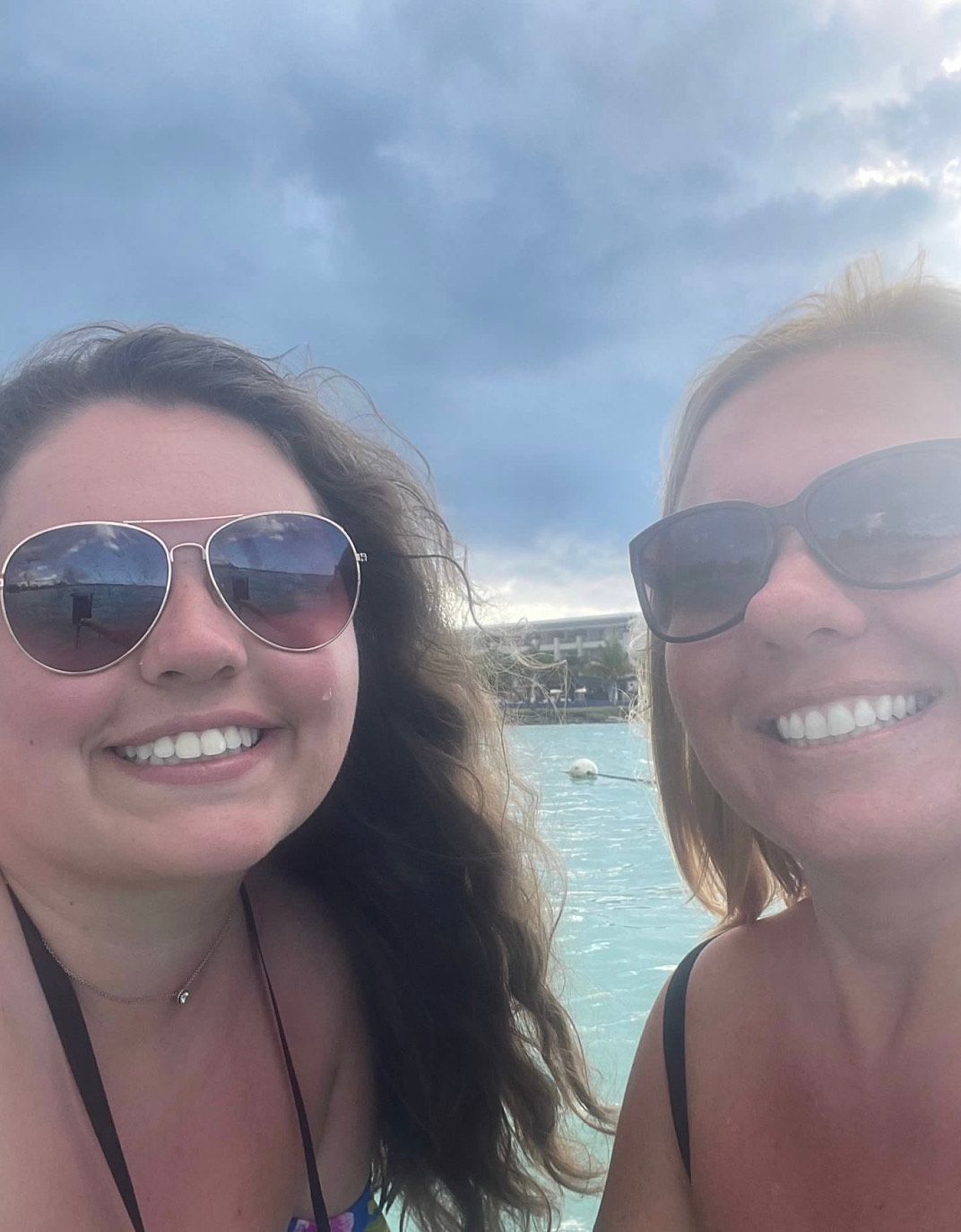 Two women wearing sunglasses are standing next to each other in front of a body of water