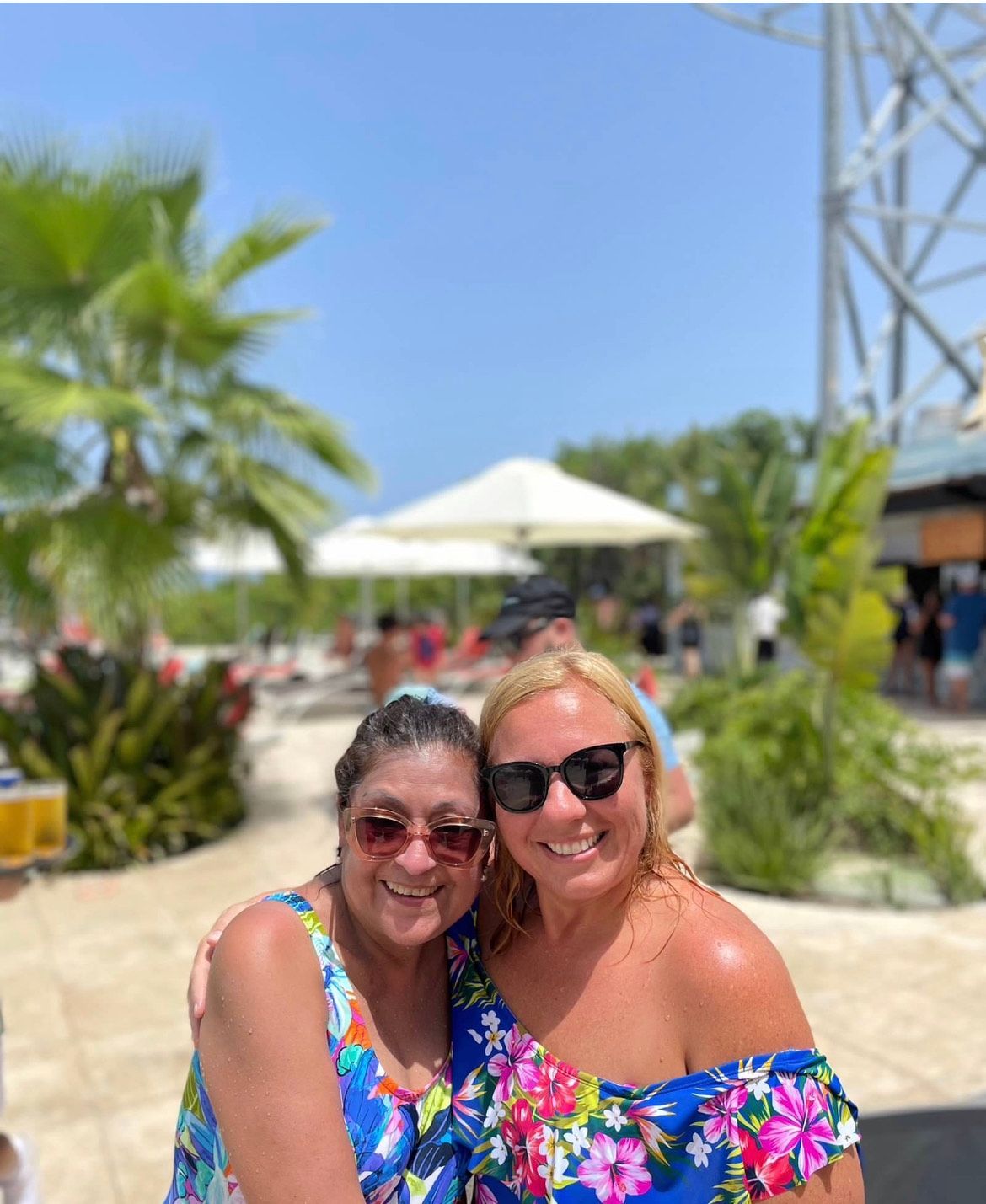 Two women wearing sunglasses and floral dresses are posing for a picture