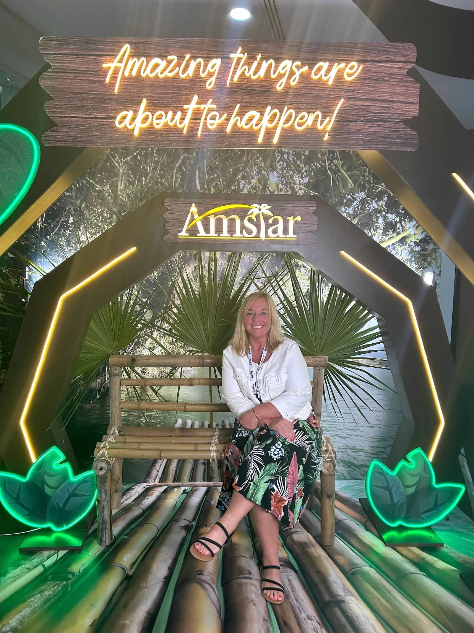 A woman is sitting on a bench in front of a sign that says amazing things are about to happen