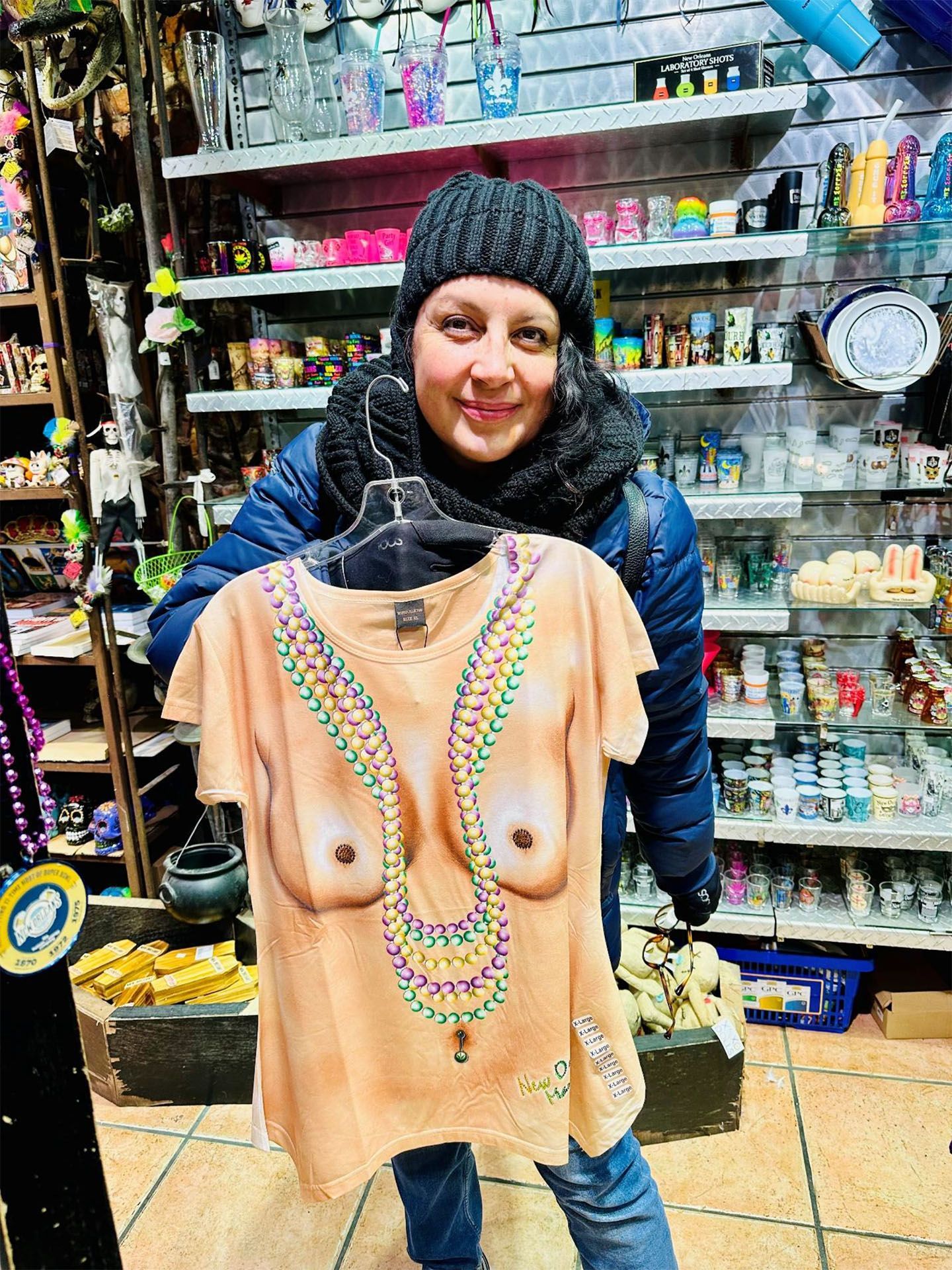 Woman holding a novelty t-shirt printed with a torso and Mardi Gras beads