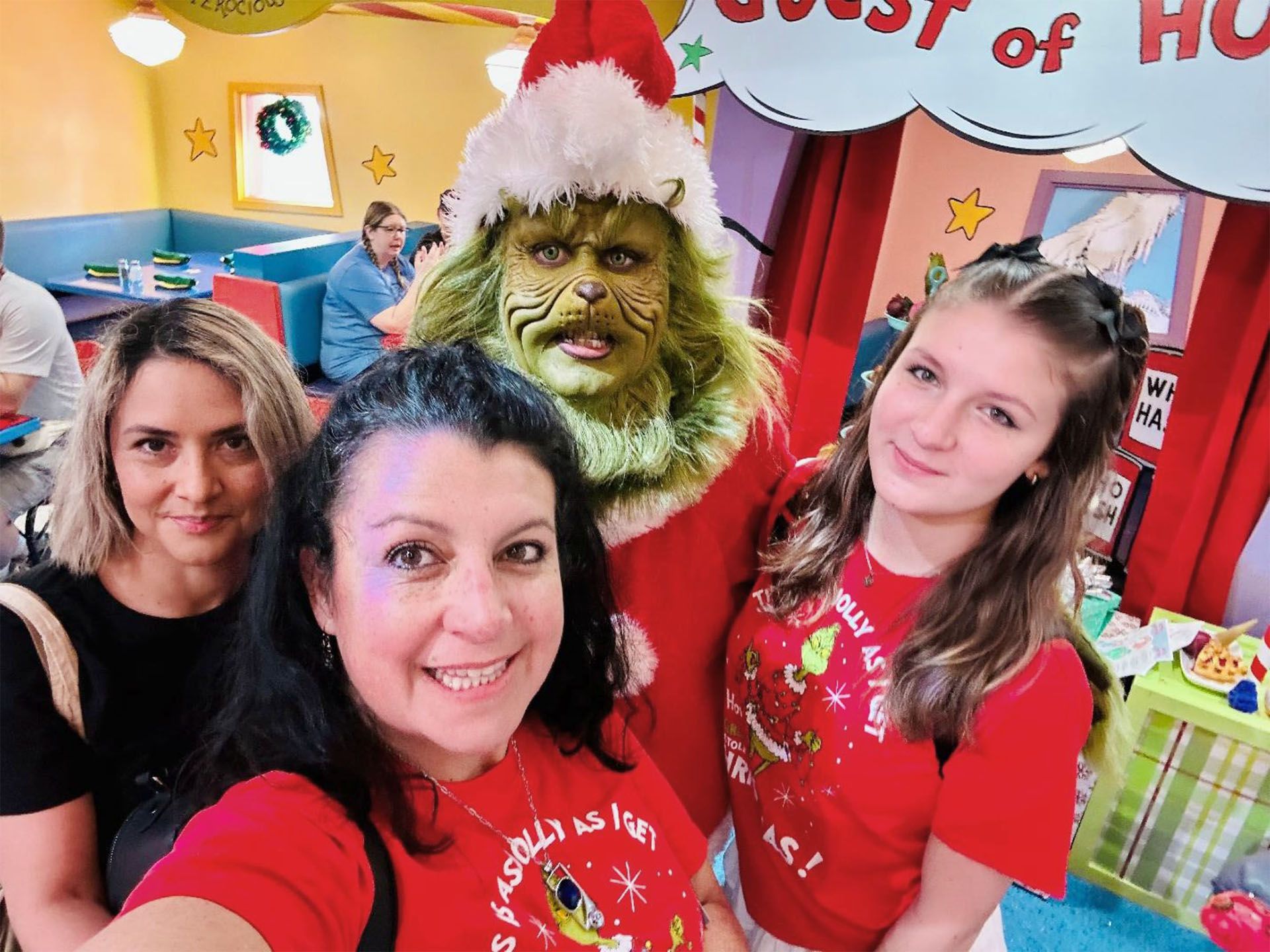 Three women pose with the Grinch character in a festive setting