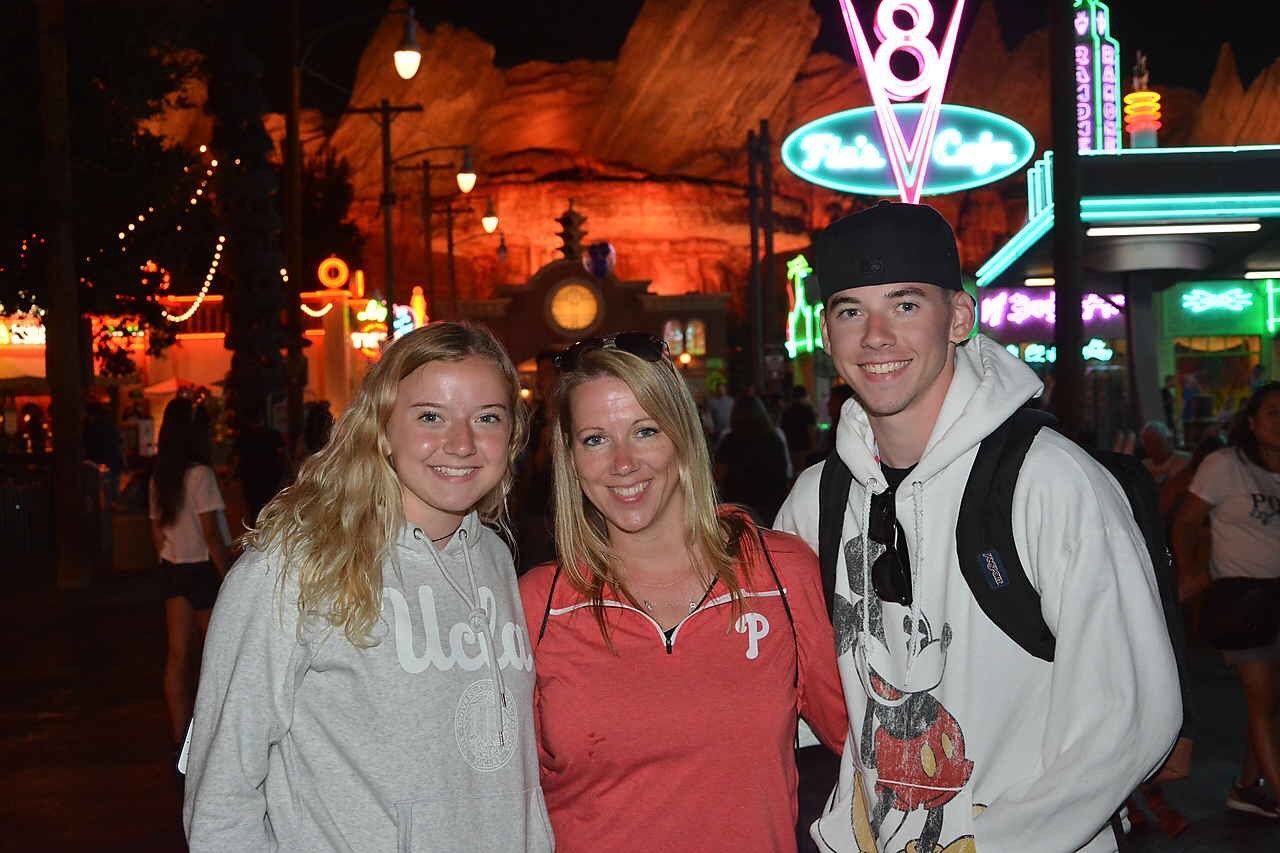 Three people smiling at Cars Land at night: two women and a man.