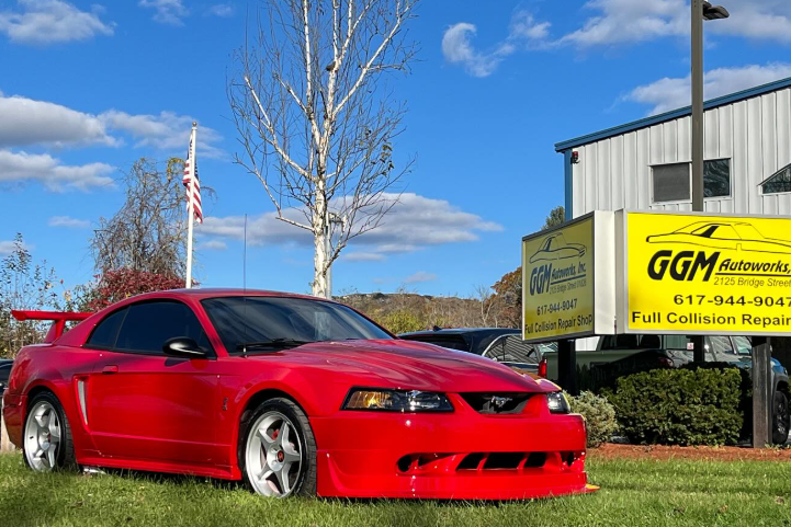 A red mustang is parked in the grass in front of a building.
