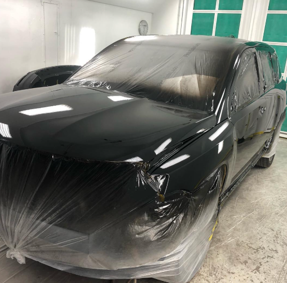 A black car is wrapped in plastic in a garage