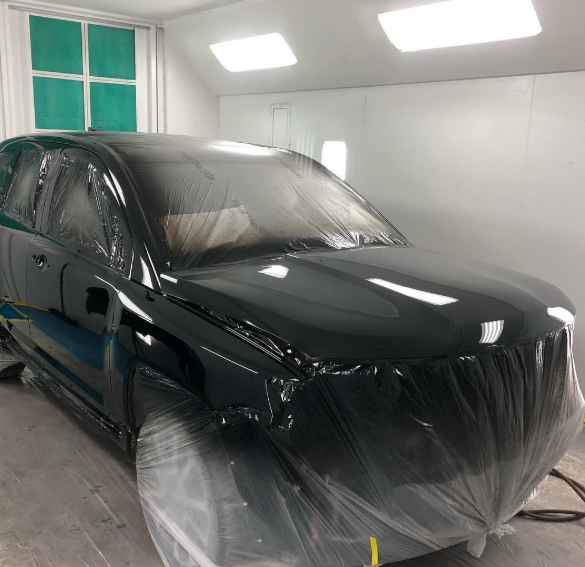 A black car is wrapped in plastic in a paint booth
