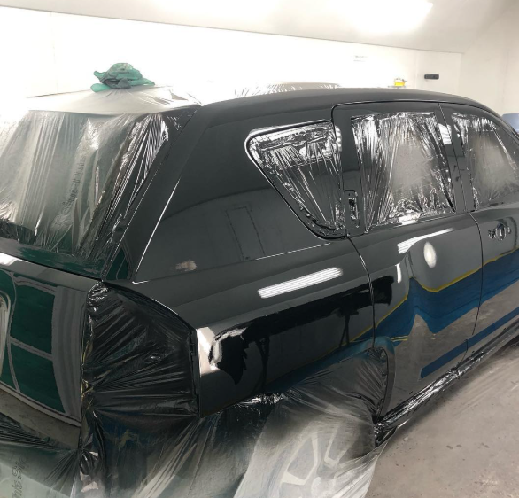 A black car is wrapped in plastic and sitting in a garage.