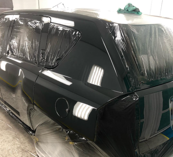 A black car is wrapped in plastic and sitting on the floor.