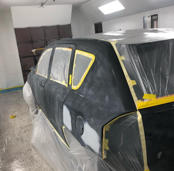 A black car is being painted in a garage