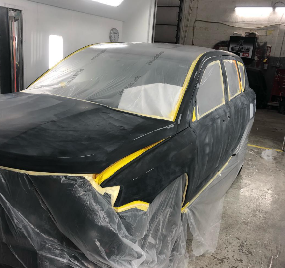 A black car is wrapped in plastic in a garage