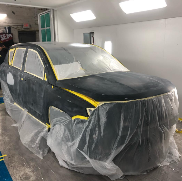 A black car is covered in plastic in a paint booth