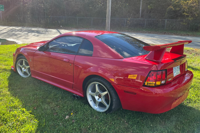 A red mustang is parked in the grass on the side of the road.