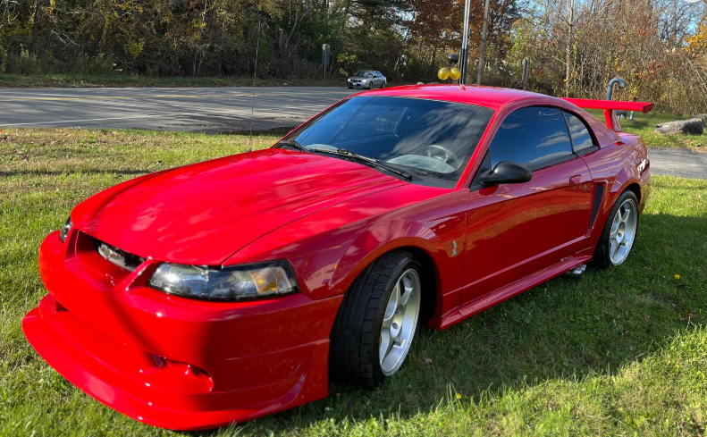 A red mustang is parked in a grassy field.