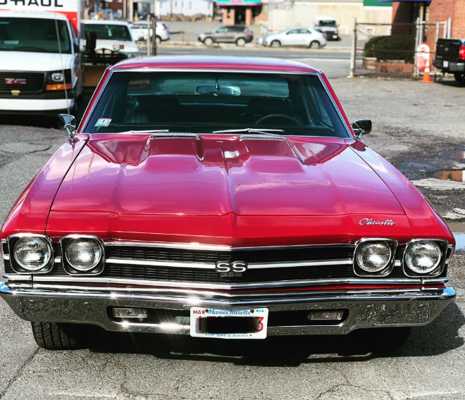 A red chevrolet is parked in front of a uhaul truck