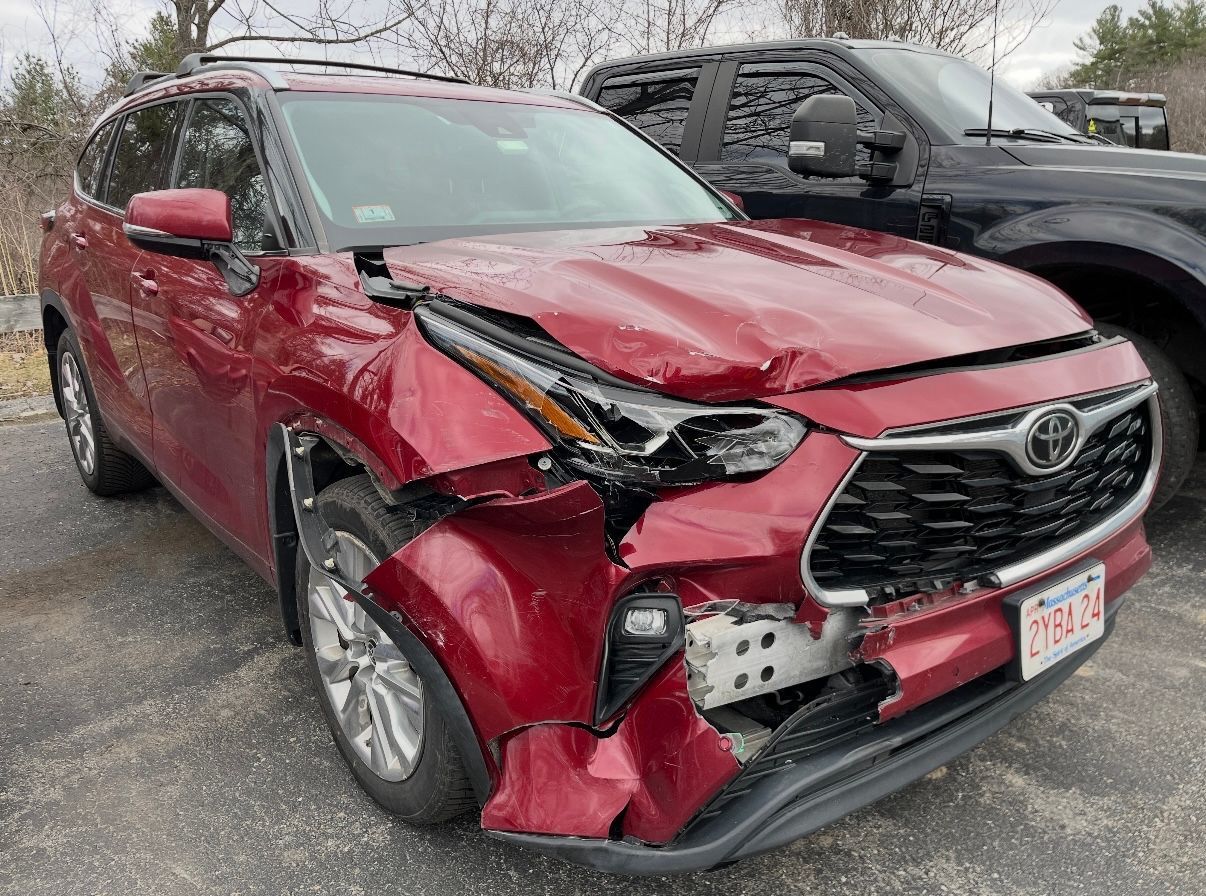 Red SUV with severe front-end crash damage in a parking lot, hood bent and bumper torn off