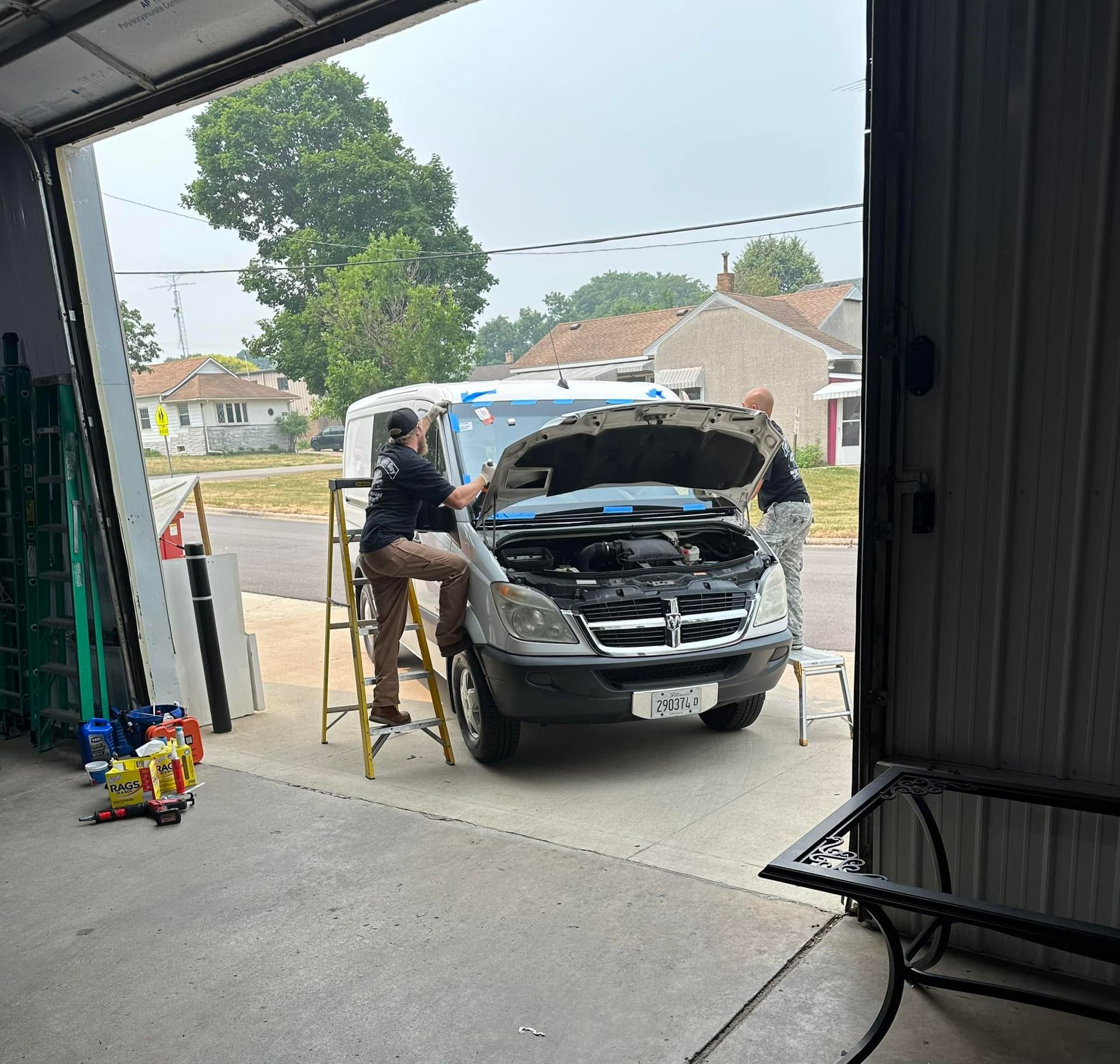 A man sitting on a ladder looking under the hood of a car