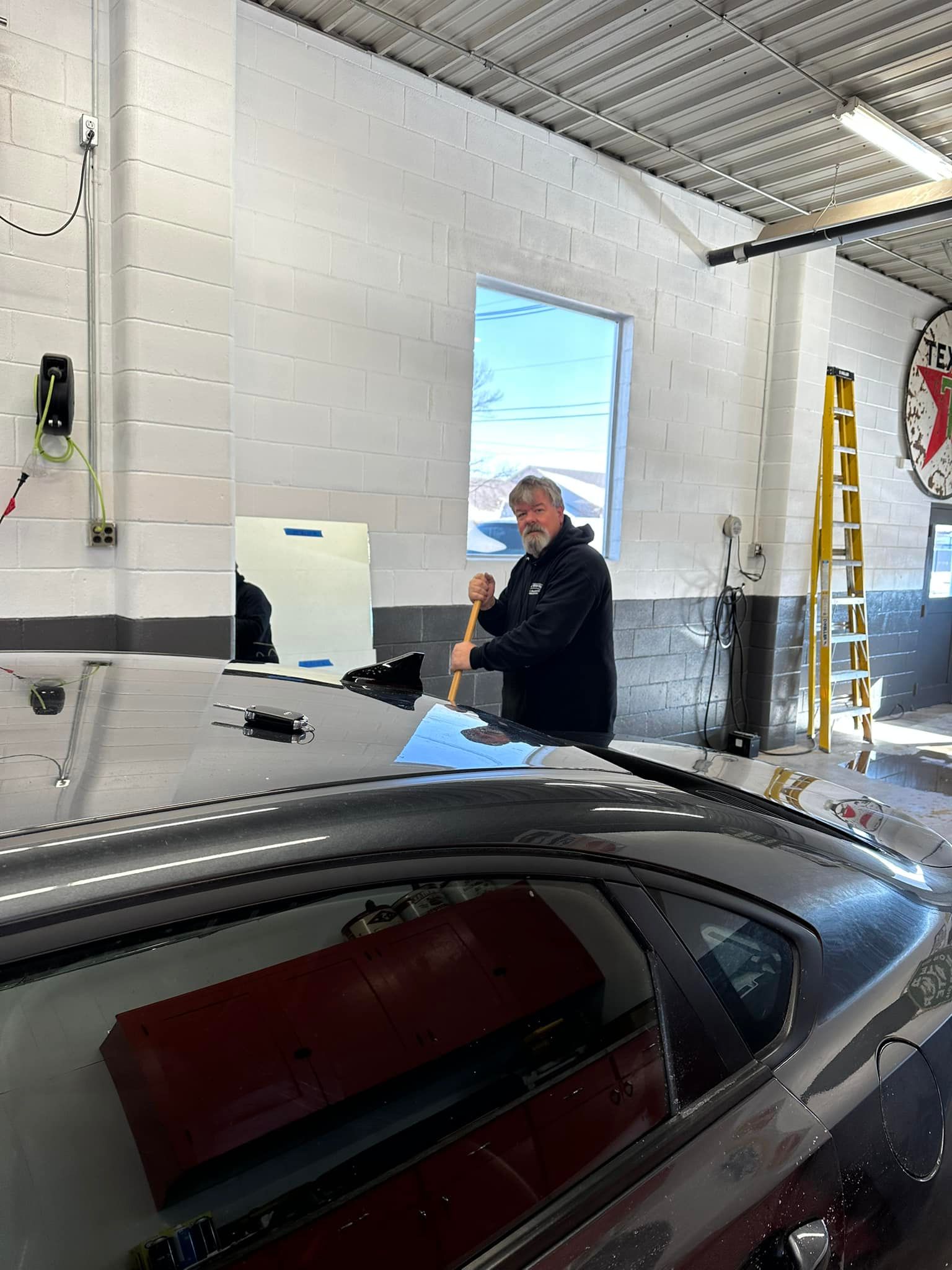 A man is working on the roof of a car in a garage.