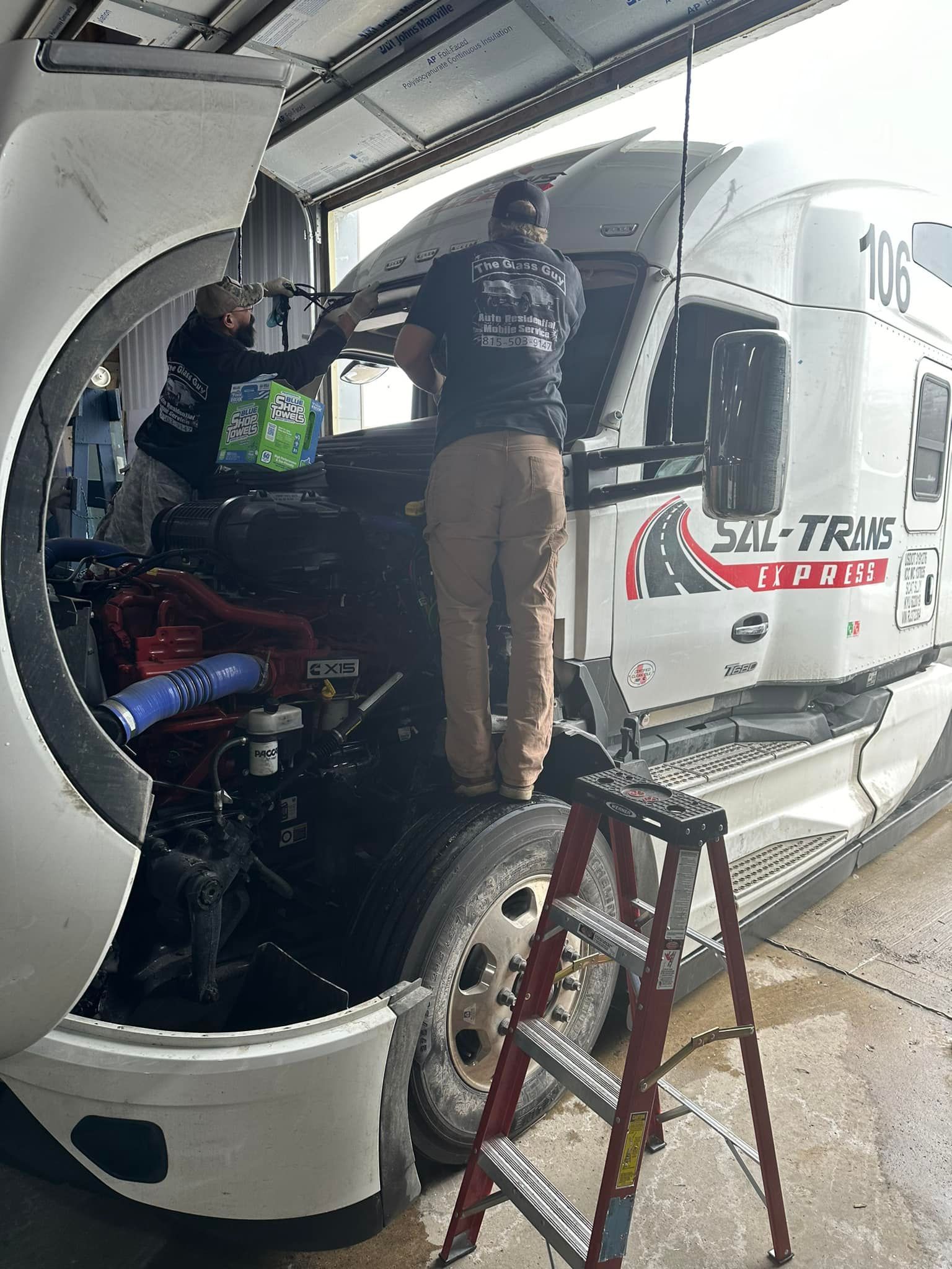 Two men are working on a semi truck in a garage.