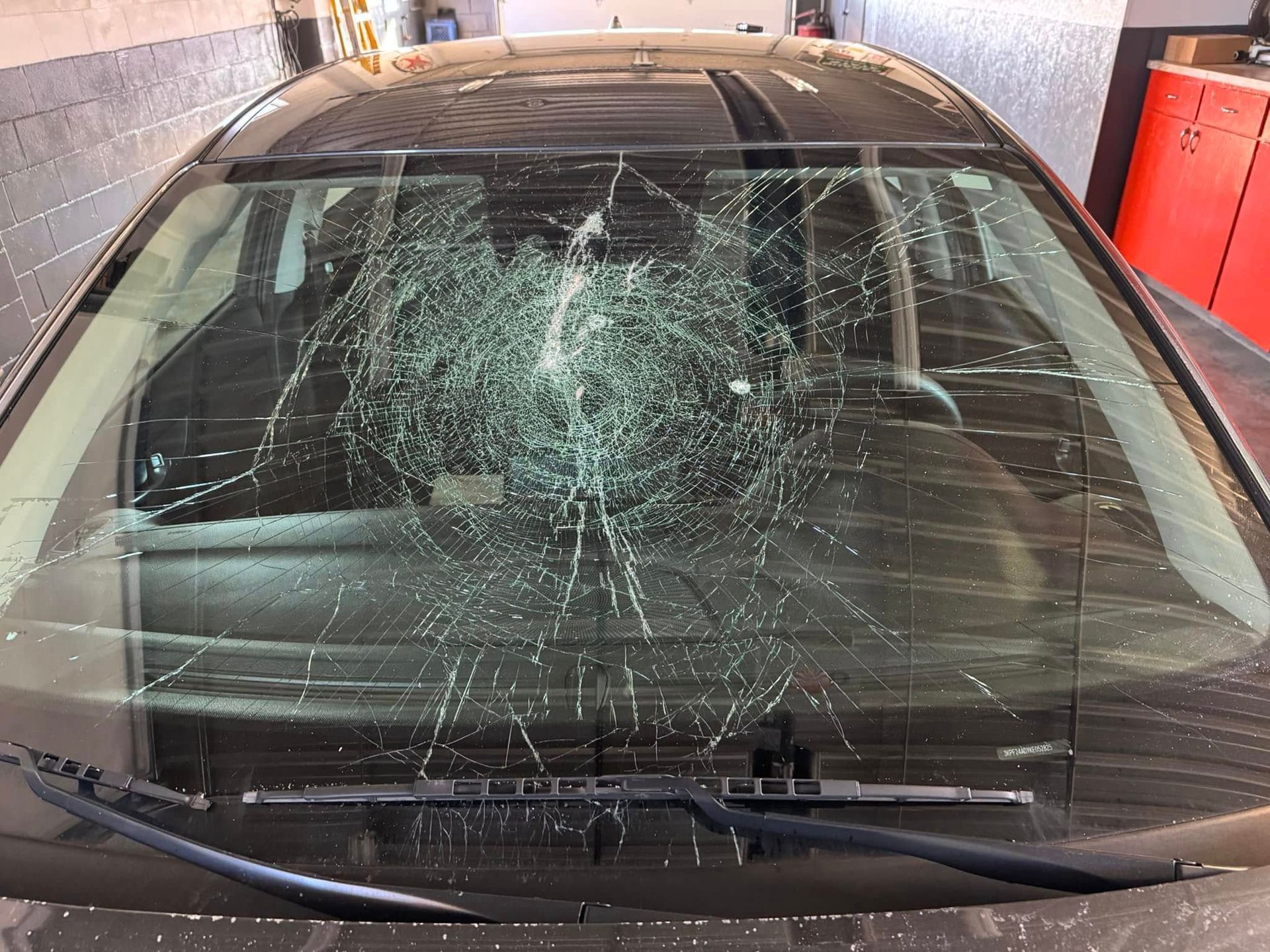 A car with a broken windshield is parked in a garage.