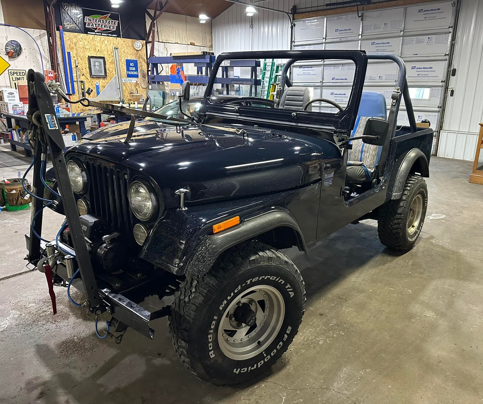 A black jeep is parked in a garage with its doors open.