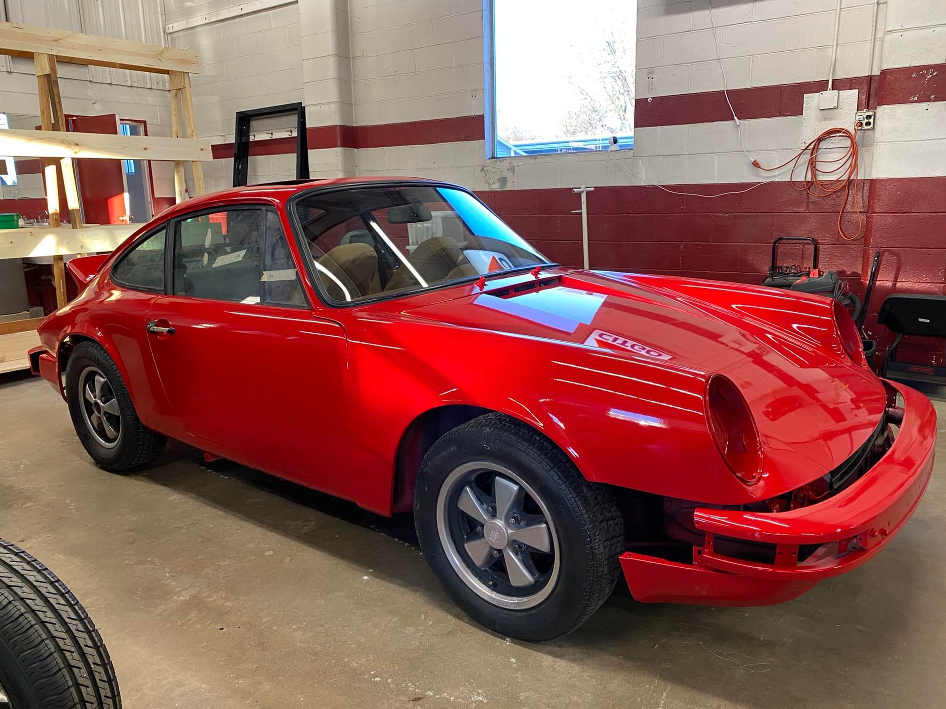 A red porsche is parked in a garage next to a window.