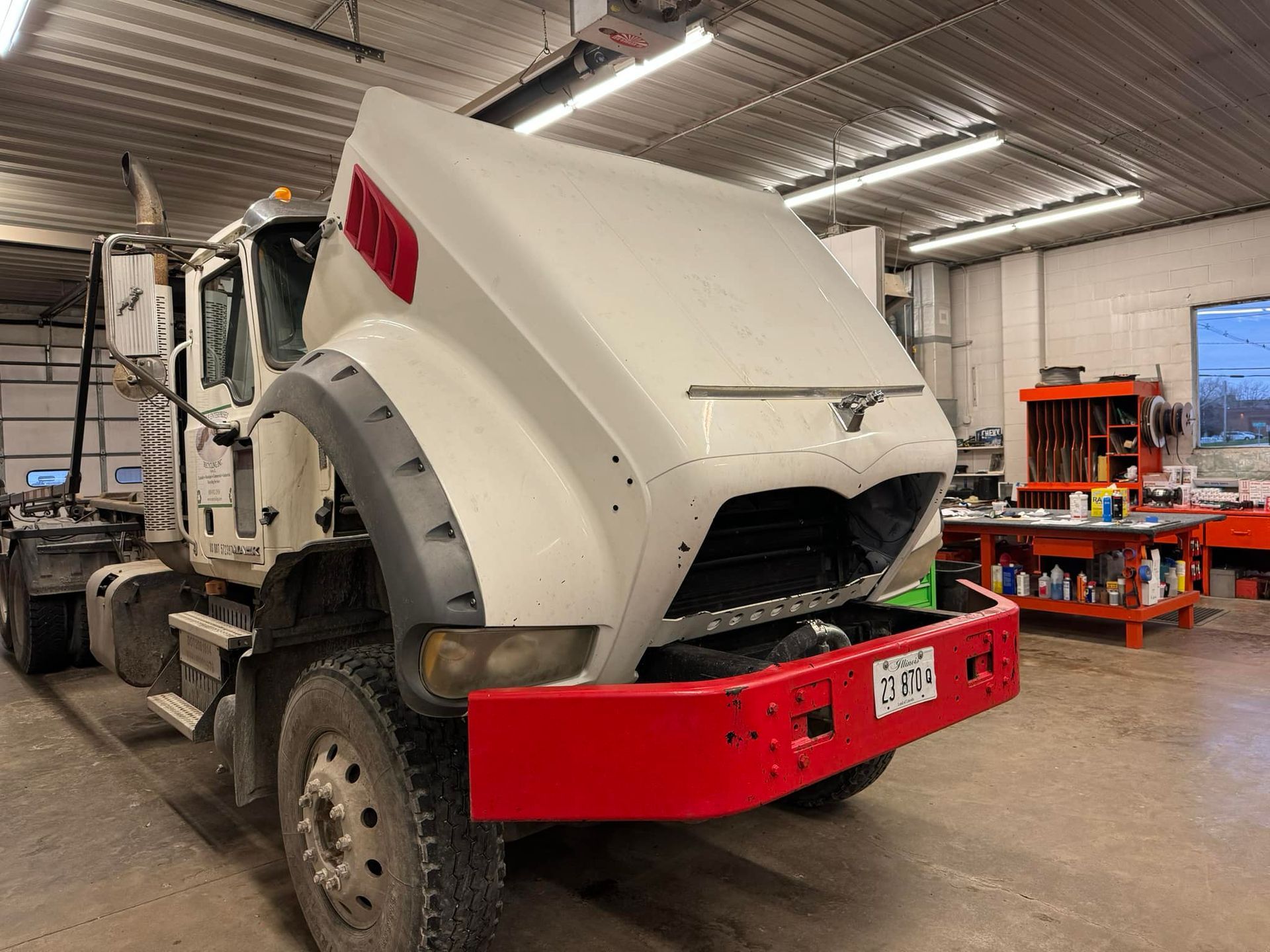 A white truck with the hood up is parked in a garage.