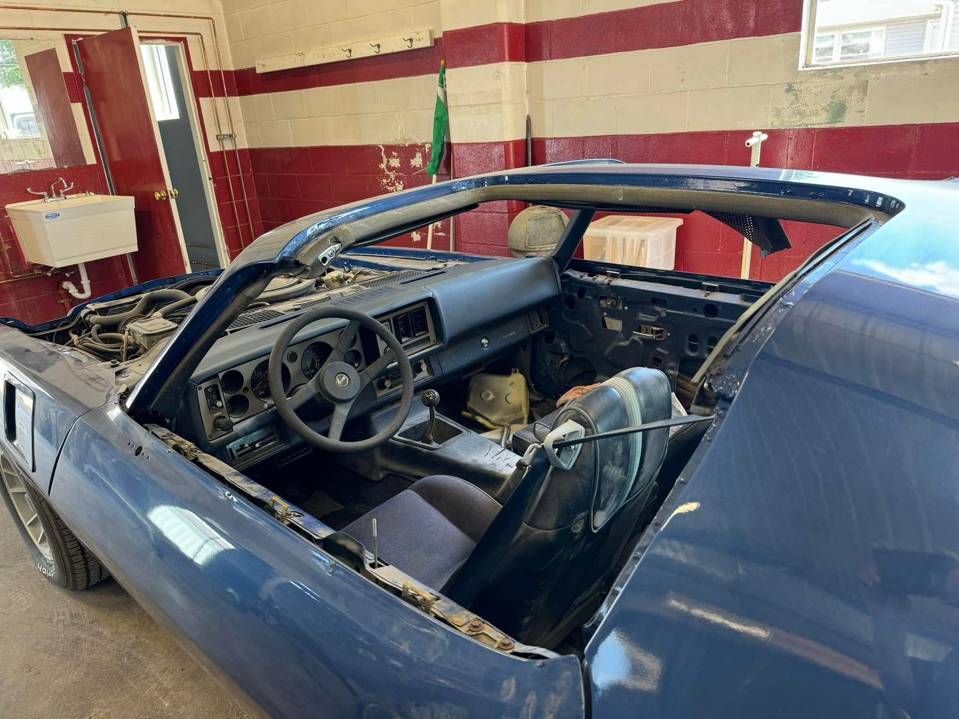 A blue car is sitting in a garage with the top down.