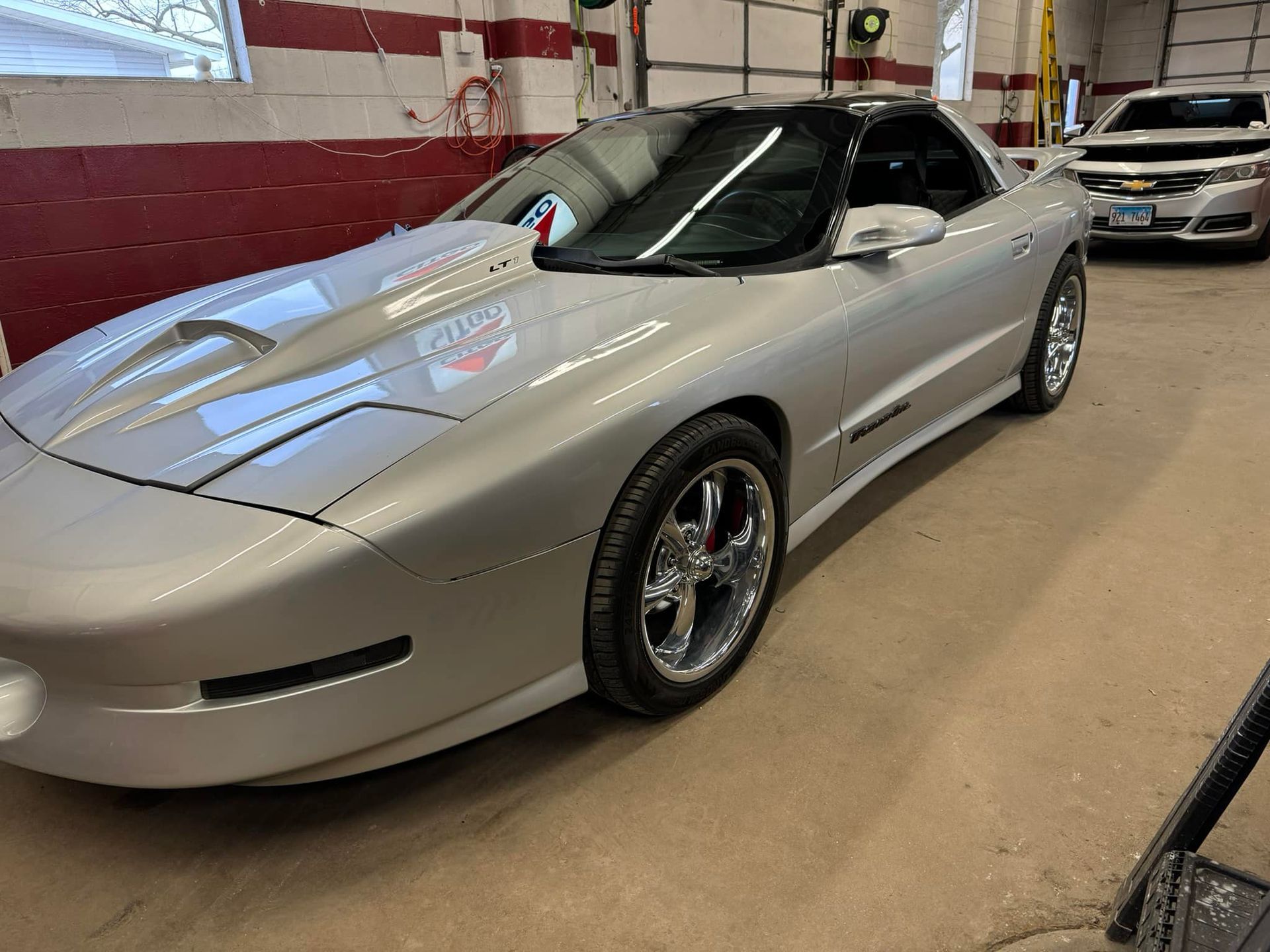 A silver car is parked in a garage next to a white car.