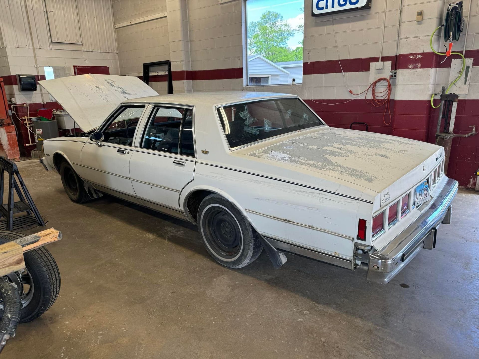 A white car with the hood up is parked in a garage.