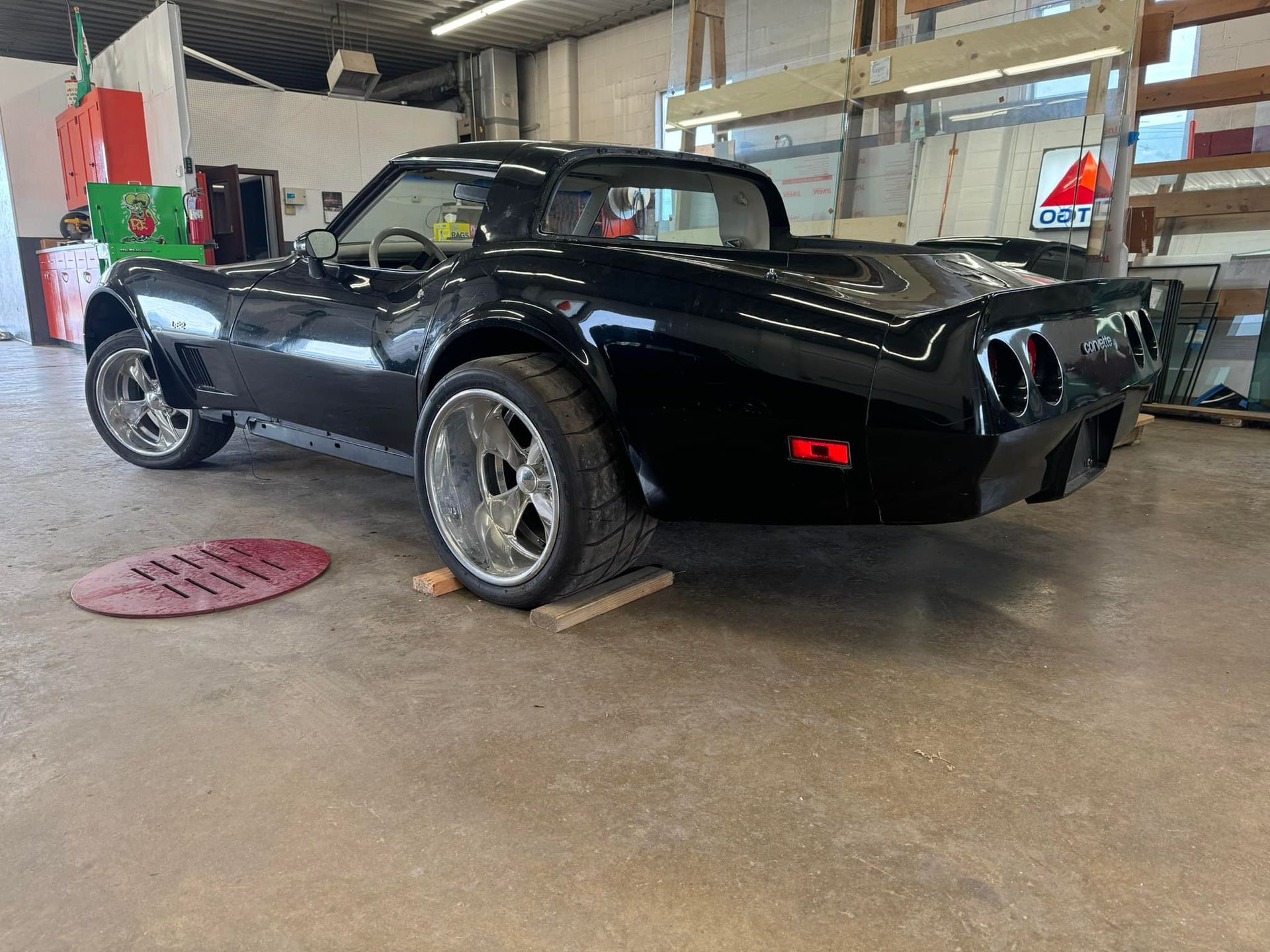 A black corvette is parked on a wooden ramp in a garage.