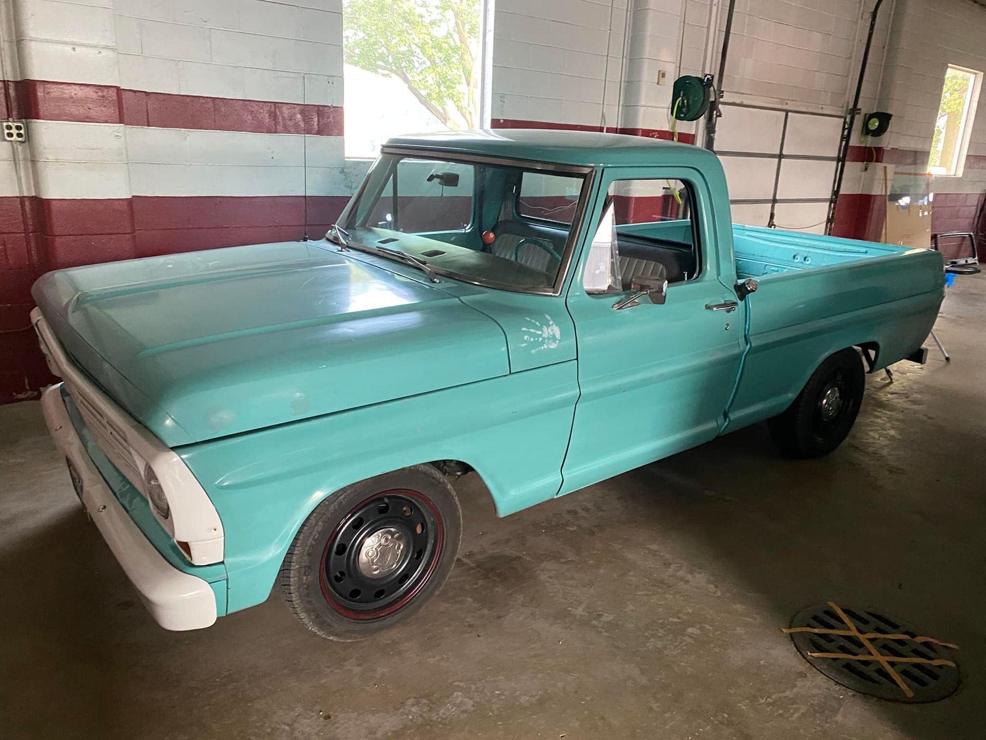 A blue truck is parked in a garage next to a window.