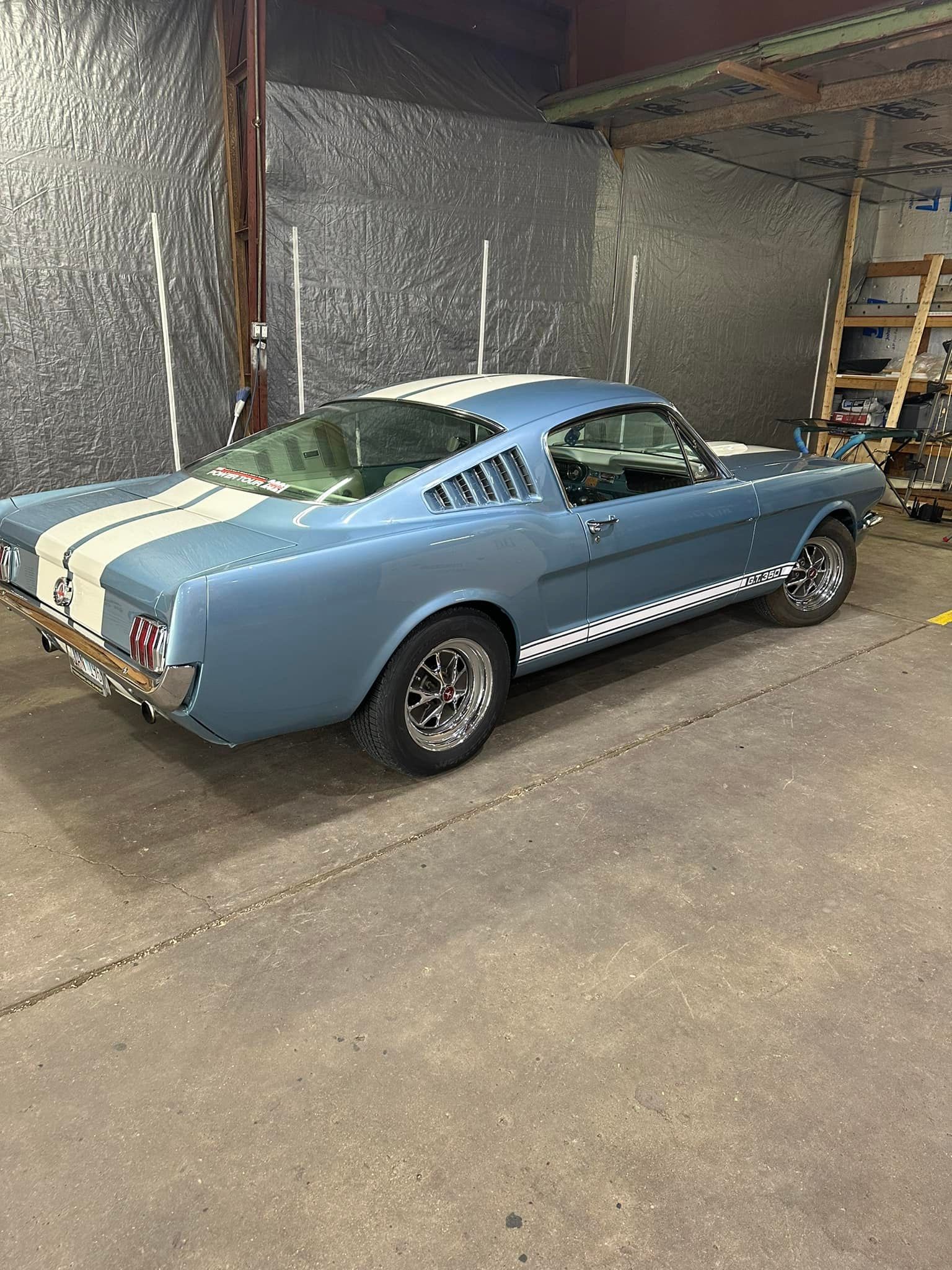 A blue and white mustang is parked in a garage.