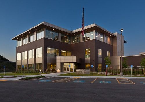 A modern three-story office building with dark brown walls and large windows under a clear blue sky at twilight.
