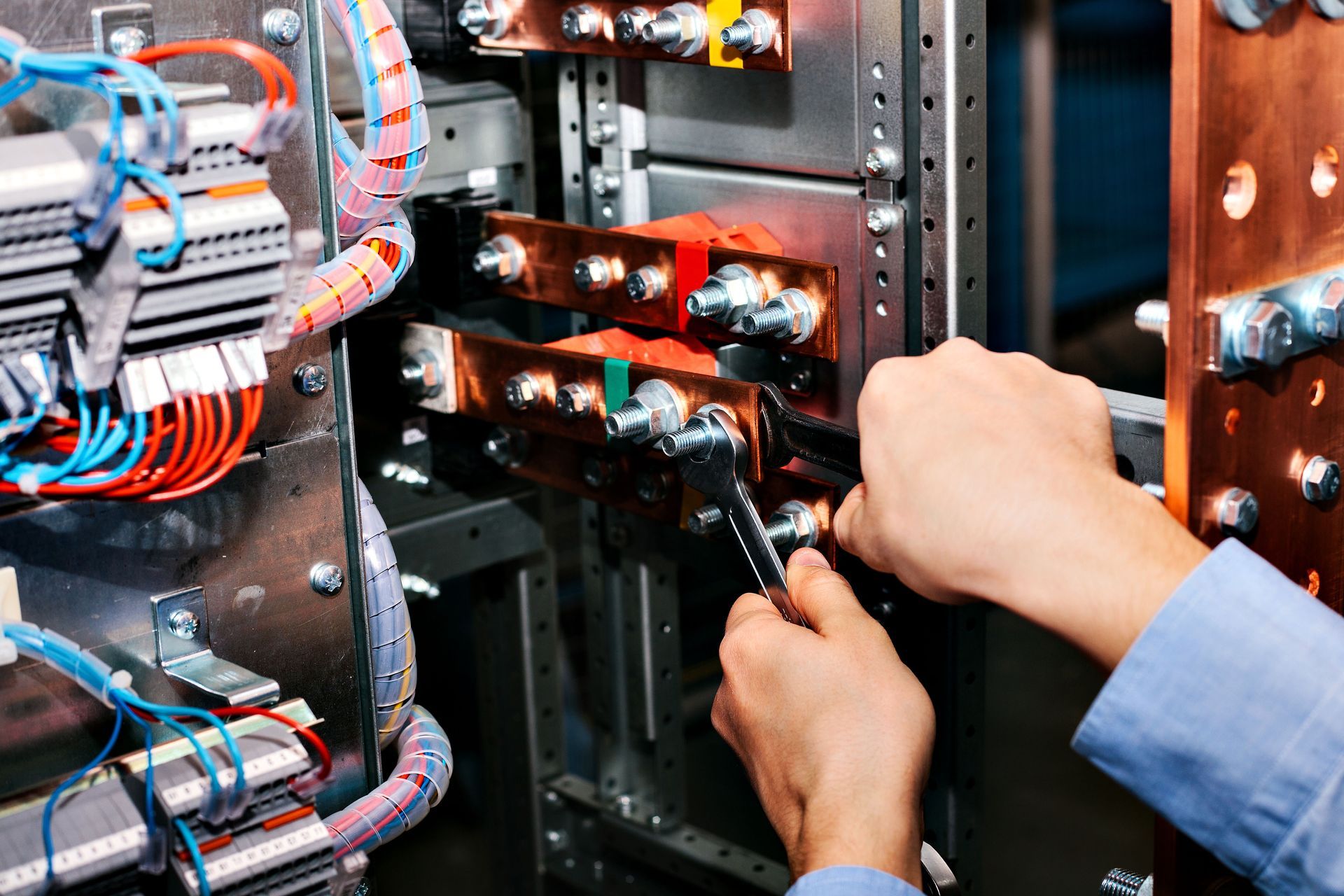 A technician uses a tool to tighten bolts on a copper electrical busbar inside a large power distribution panel.