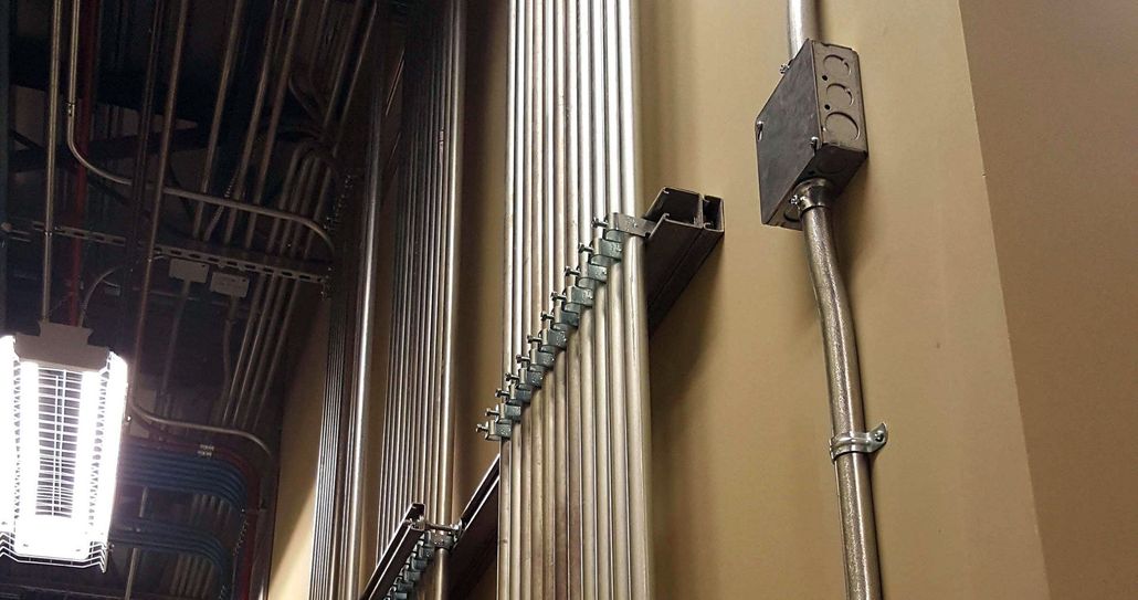 Electrical conduits mounted on a wall with metal channels and straps in an industrial or commercial setting.