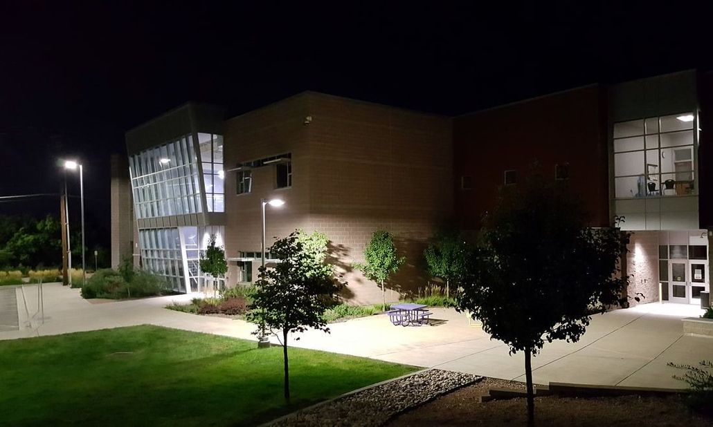 Modern building exterior at night with lit glass entrance, trees, and lawn under streetlights