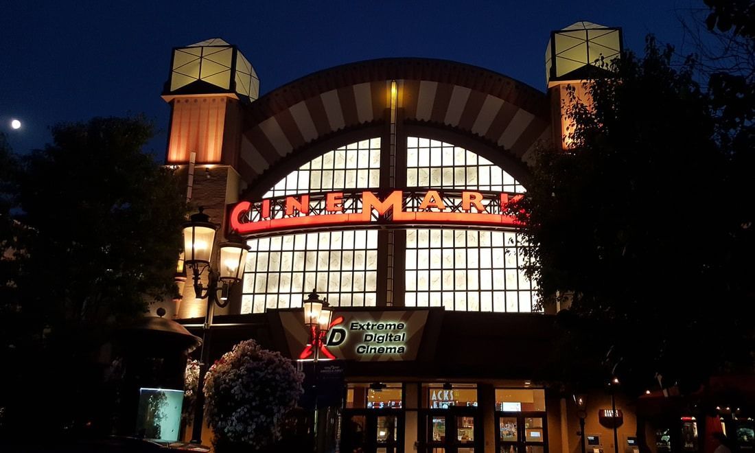 The Cinemark movie theater entrance at night with illuminated red signage, glass windows, and architectural towers.