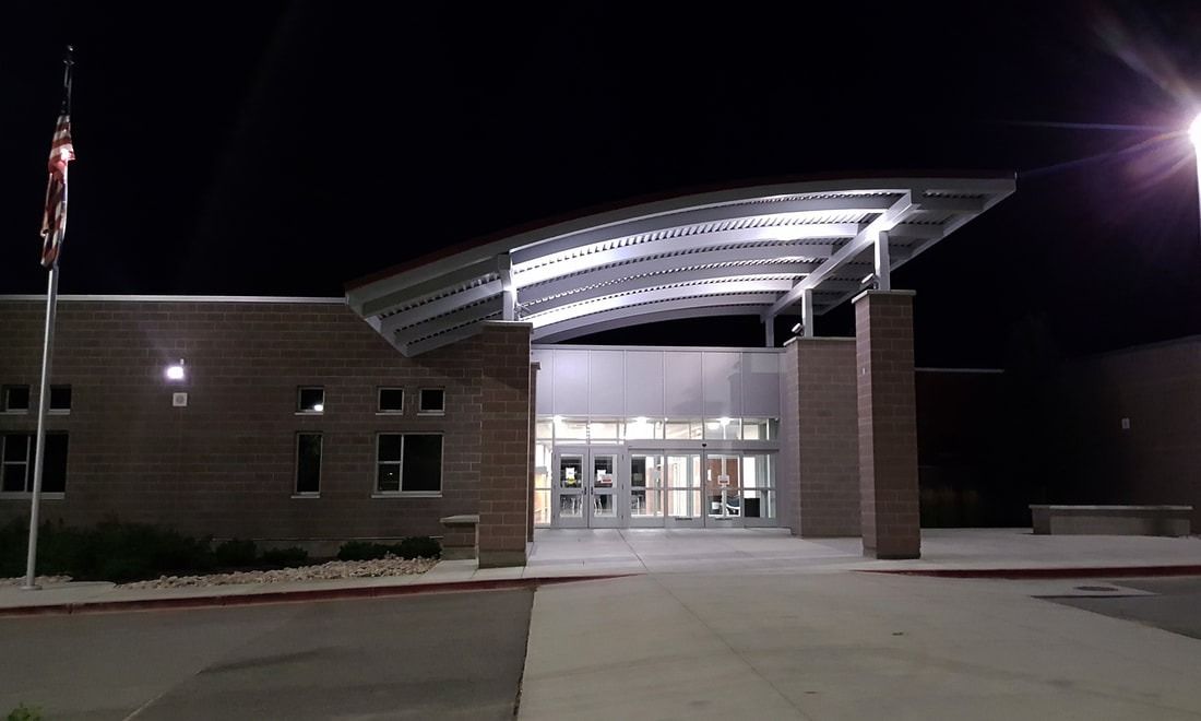Exterior of a modern school entrance with a curved metal canopy and brick walls, illuminated at night.