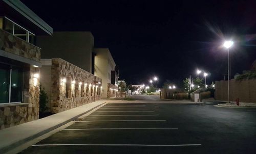 A modern building with a stone-accented facade stands beside a parking lot illuminated by tall streetlights at night.