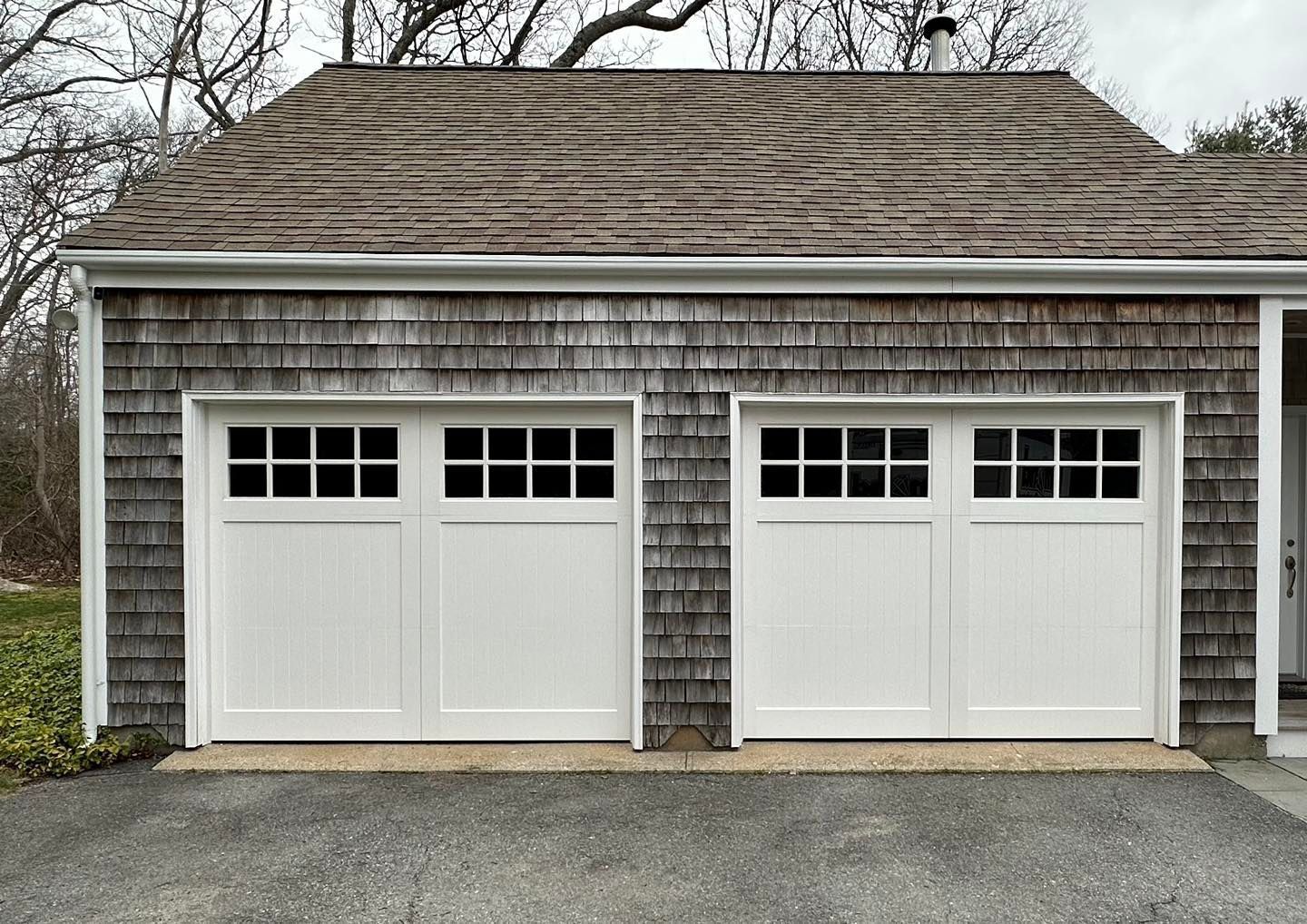 A garage with two white garage doors and a shingle roof
