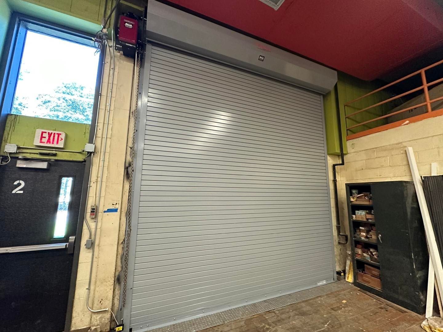 A large garage door is open in a room with a red exit sign