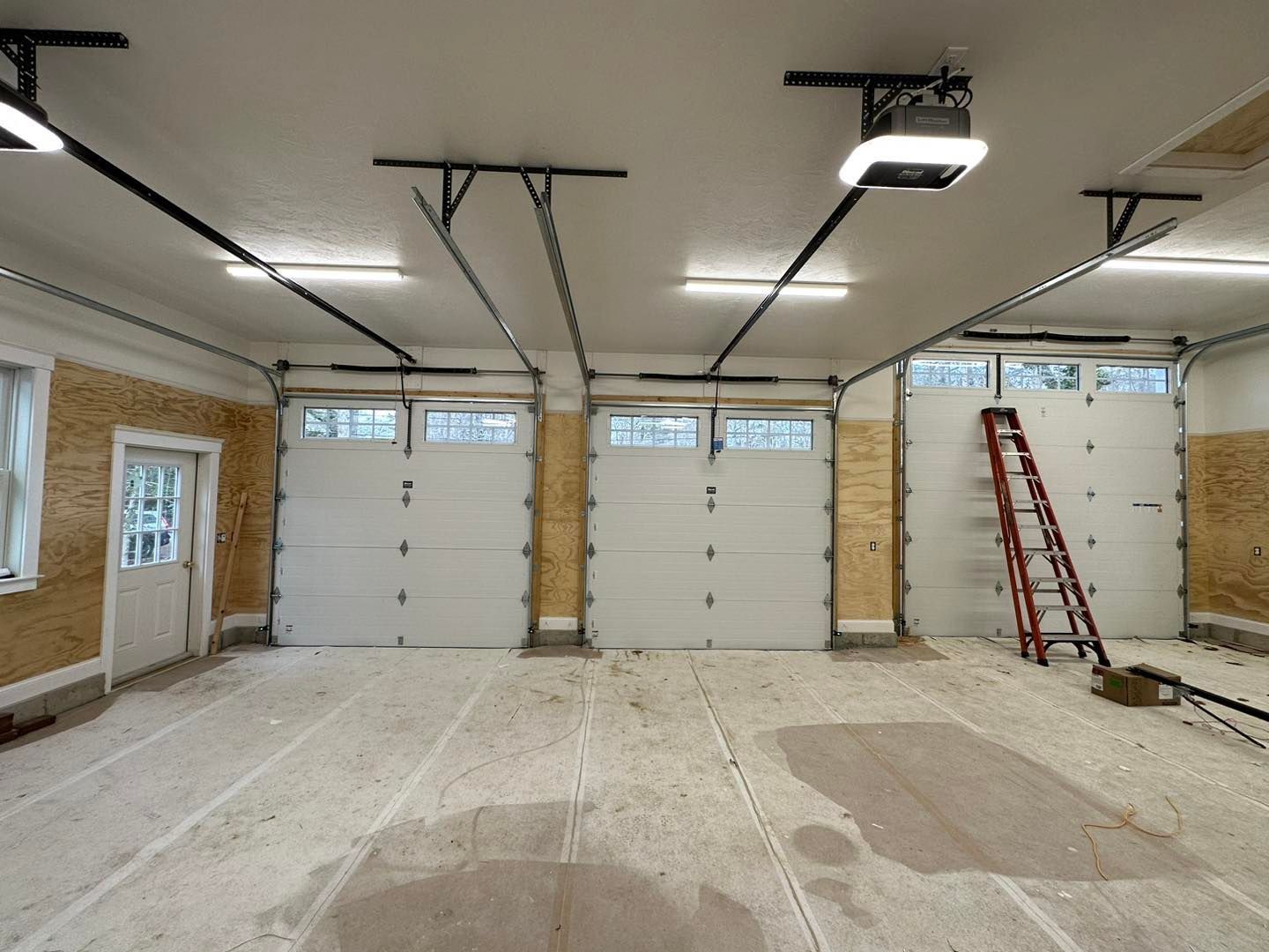 An empty garage with three garage doors and a ladder