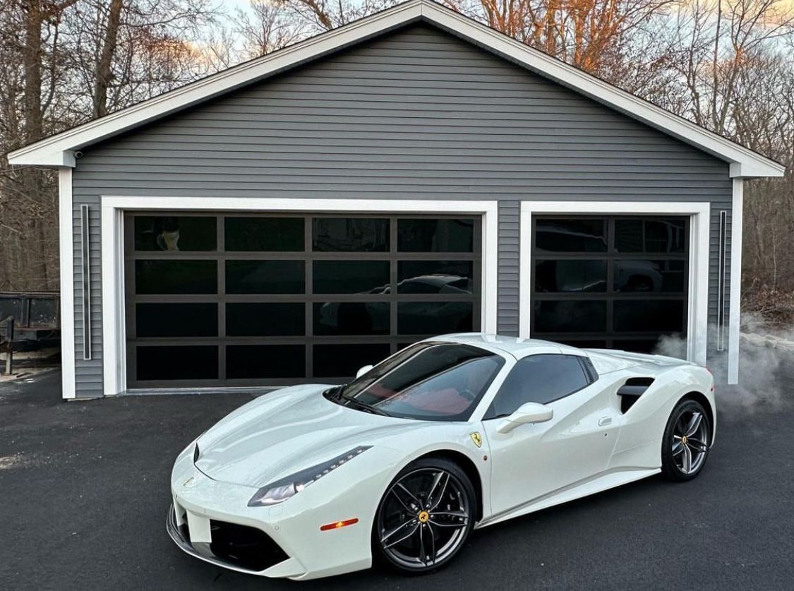 A white ferrari 488 gtb is parked in front of a garage