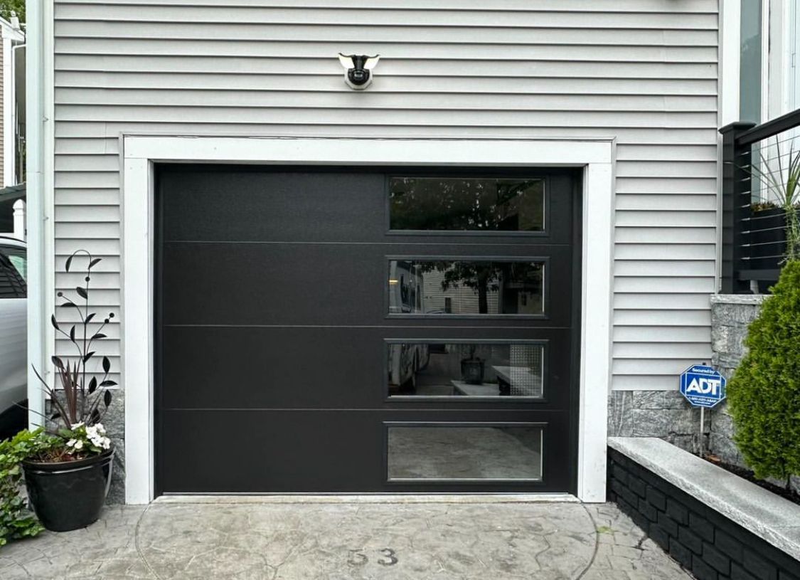 A black garage door is sitting in front of a white house