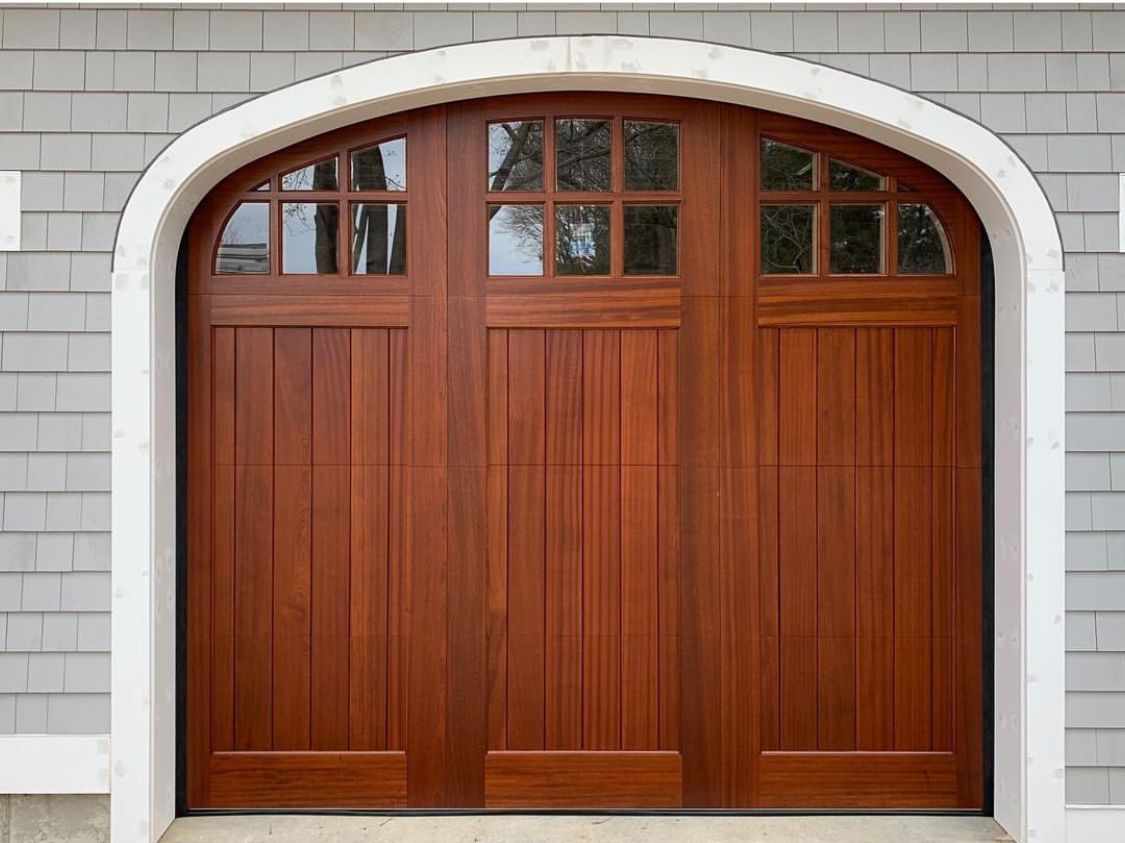 A wooden garage door with arched windows on a brick building