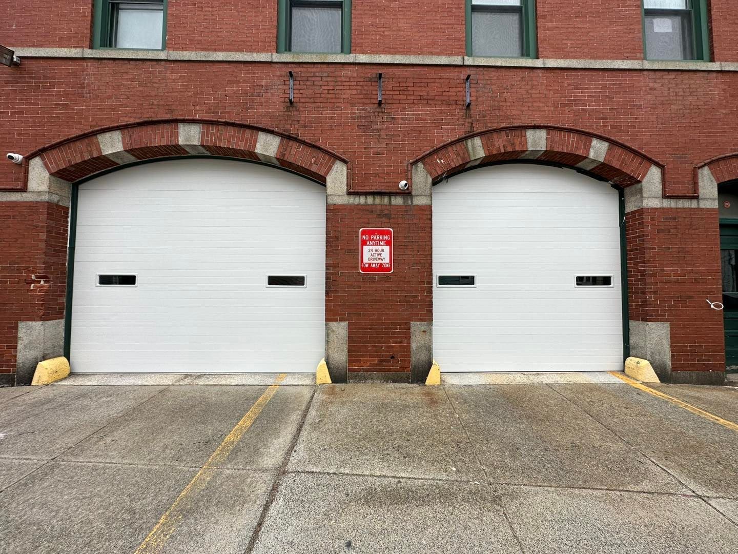 Two white garage doors are sitting in front of a brick building.