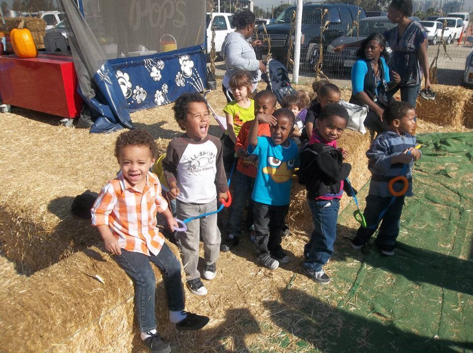 A group of children are standing around hay bales at a pumpkin patch.