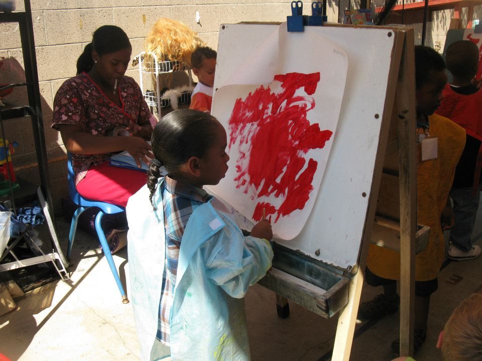 A little girl is painting on a white board with red paint.